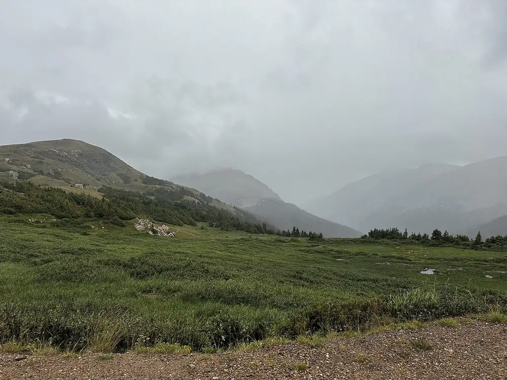 Gravel Old Fall River Road running beside an alpine meadow below misty Colorado peaks